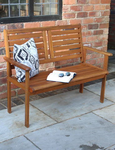 Wooden garden bench with slatted backrest, patterned cushion, and book on patio