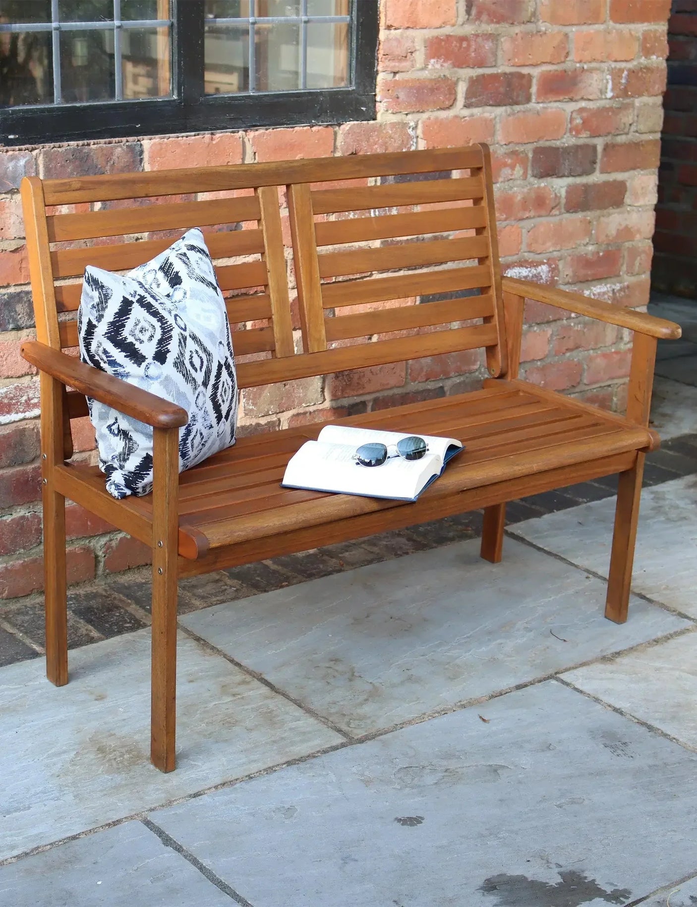 Wooden garden bench with slatted backrest, patterned cushion, and book on patio