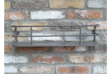 Grey metal wall-mounted shelf with raised rails, displayed against a rustic multicolored brick wall.