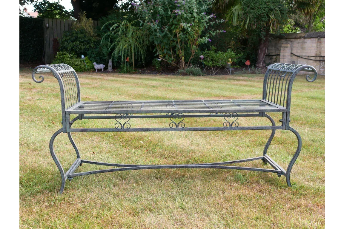 Metal garden bench with ornate scroll armrests and slatted seat on grass lawn
