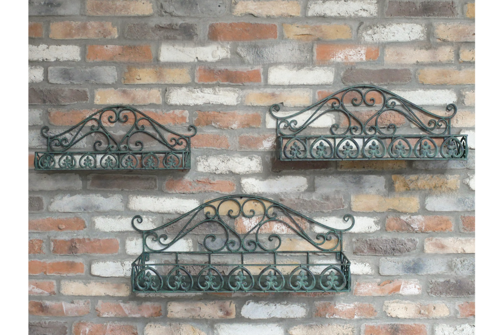 Set of 3 green metal wall shelves with ornate scrollwork detail, mounted on a rustic brick wall, viewed from the front.