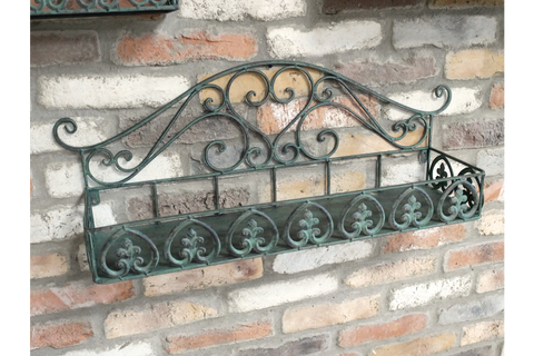 Greenish-blue metal wall shelf with ornate scrollwork, mounted at an angle on a brick wall background.