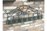 Greenish-blue metal wall shelf with ornate scrollwork, mounted at an angle on a brick wall background.
