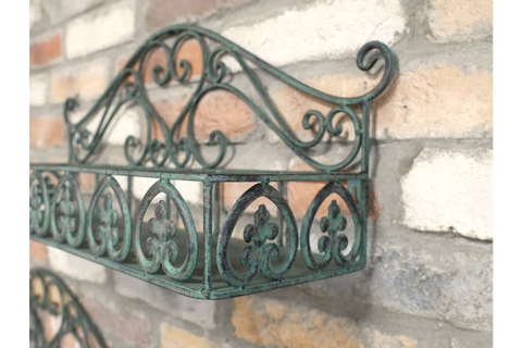 Green metal wall shelf with ornate scrollwork, mounted on a rustic brick wall, angled close-up view.