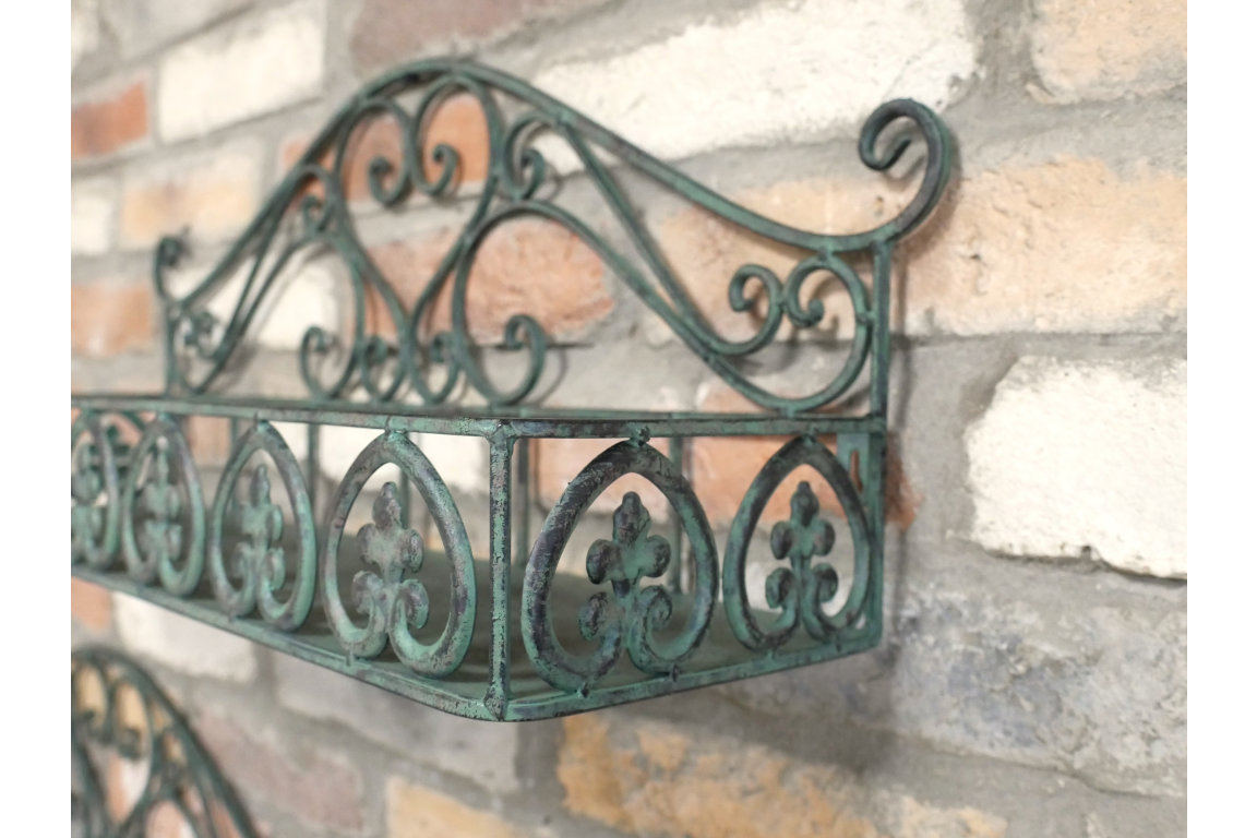 Green metal wall shelf with ornate scrollwork, mounted on a rustic brick wall, angled close-up view.
