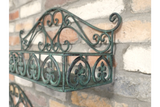 Green metal wall shelf with ornate scrollwork, mounted on a rustic brick wall, angled close-up view.
