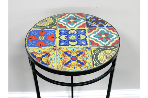 Round side table with multicolored patterned tile top and black metal frame, shown from an angled top view.
