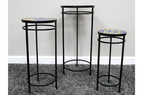 Set of 3 black metal side tables with colorful mosaic tile tops, displayed on gray carpet against a white wall.