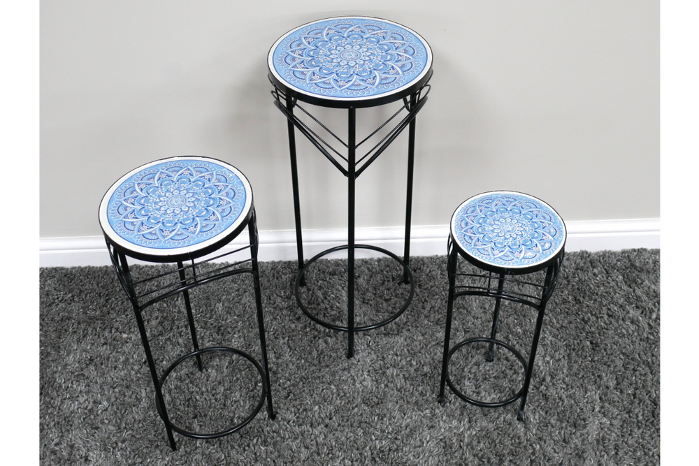 Set of three black metal side tables with round blue and white patterned tops, displayed on gray carpet.