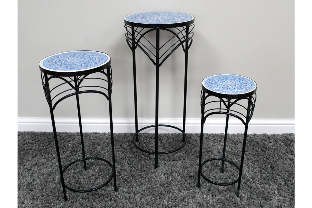 Set of three black metal side tables with blue patterned round ceramic tops, shown at front angle on gray carpet.