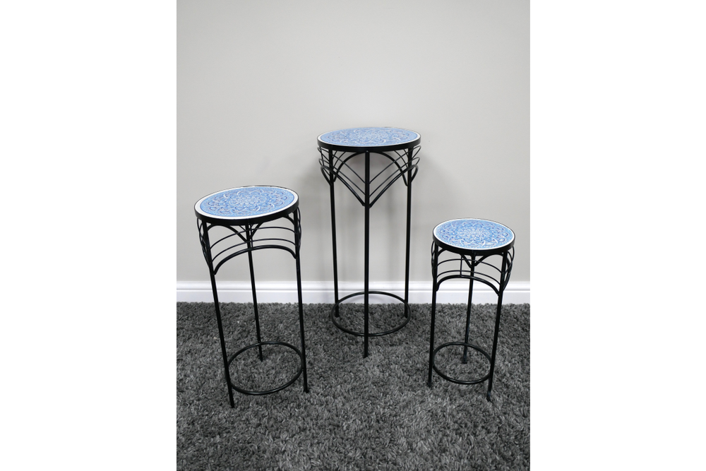 Set of 3 round side tables with black metal legs and blue patterned ceramic tops, shown on gray carpet against white wall.