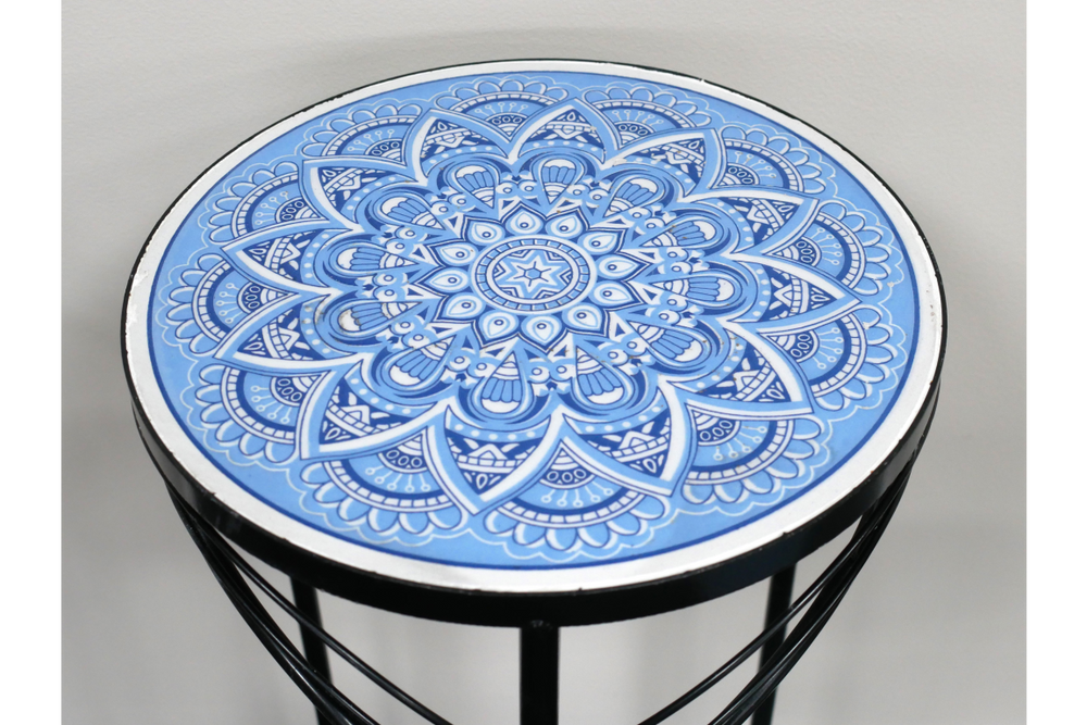 Round side table with black metal frame and blue and white intricate mandala tile top, angled view.
