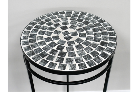 Round side table with black and white mosaic tile top and black metal legs, angled view against white wall.