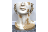 White and gold distressed ceramic head-shaped side table on gray carpet with white baseboard background