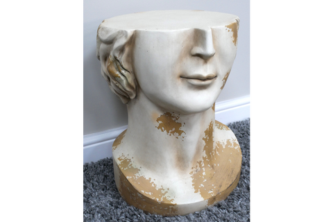 White and gold distressed ceramic head-shaped side table shown from front angle on gray carpet