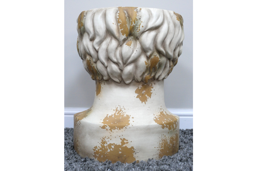 Round head-shaped side table in distressed white and gold finish, shown from rear on grey carpet.