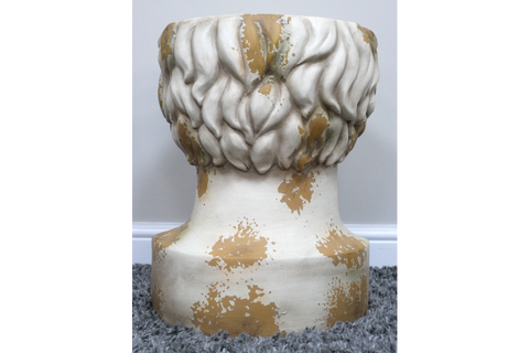 Round head-shaped side table in distressed white and gold finish, shown from rear on grey carpet.