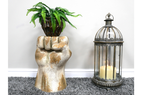 Side table shaped like a raised fist in distressed white and gold finish with a potted fern on top, next to a decorative