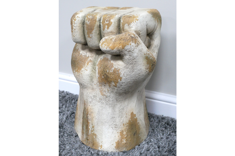 Side table shaped like a clenched fist, weathered white and beige finish, displayed on gray carpet near white wall.