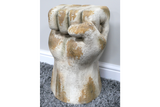 Side table shaped like a clenched fist, weathered white and beige finish, displayed on gray carpet near white wall.