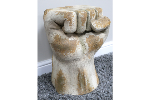 Fist-shaped side table in distressed white and beige finish, textured surface, shown on gray carpet with white baseboard