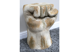 Fist-shaped side table in distressed white and beige finish, textured surface, shown on gray carpet with white baseboard