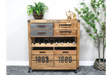 Wooden wine cabinet with metal and wood drawers, open bottle rack, and numbered crate compartments, shown in a room setting.