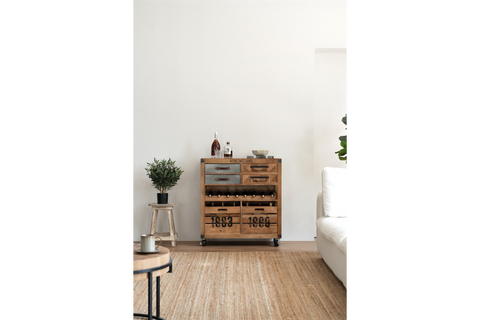 Wooden wine cabinet with metal accents, drawers, shelves, and wheels in a modern living room setting.