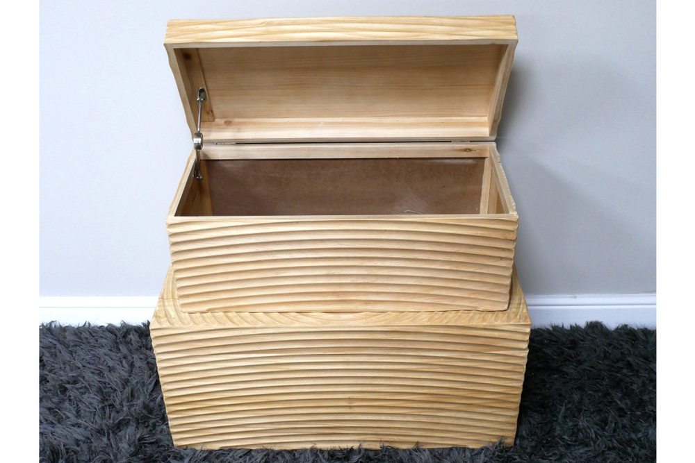 Set of two light wood storage boxes with horizontal grooves, one open showing interior, placed on dark grey carpet.