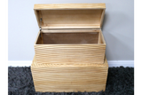 Set of two light wood storage boxes with horizontal grooves, one open showing interior, placed on dark grey carpet.