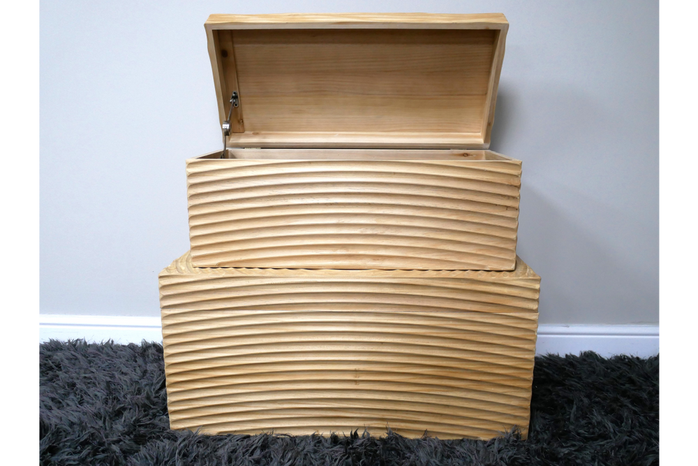 Set of two light wood storage boxes with carved wave patterns, one open, stacked on dark grey shag carpet.