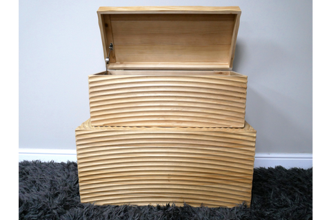 Set of two light wood storage boxes with carved wave patterns, one open, stacked on dark grey shag carpet.