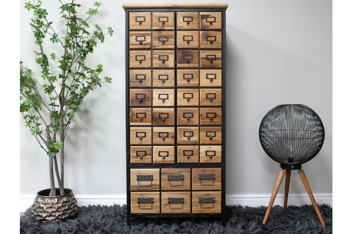 Tall wooden storage cabinet with multiple small drawers, black metal frame, standing on dark shaggy rug between plant and