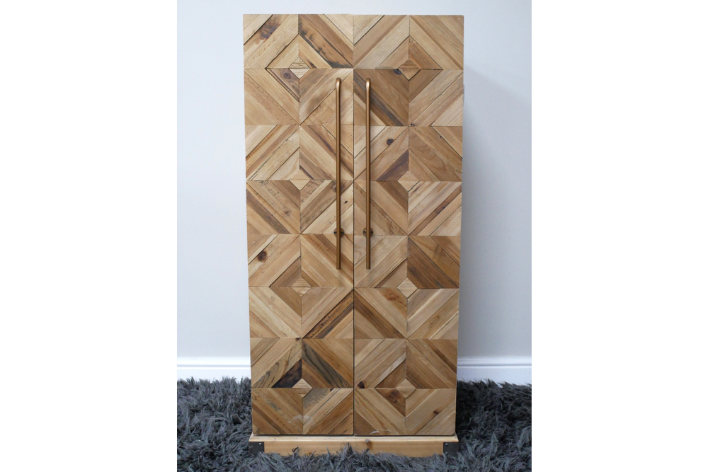 Wooden wine cabinet with geometric square pattern front, vertical metal handles, standing on gray shaggy rug.