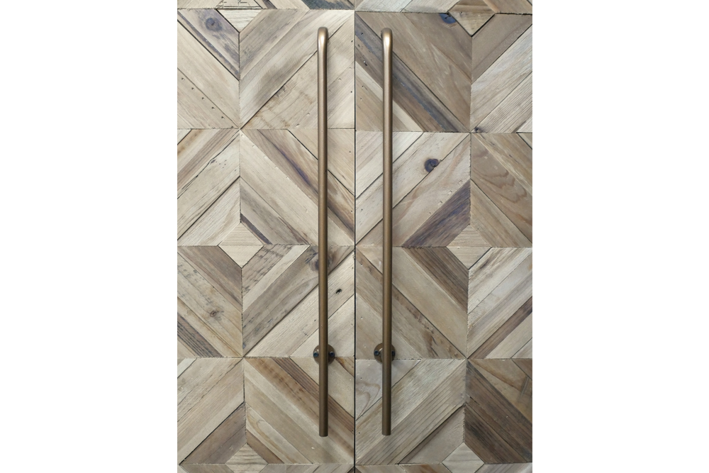 Wine cabinet with geometric patterned wood doors in natural tones and tall bronze handles, front view.