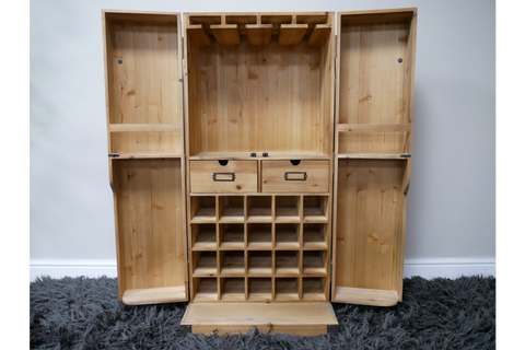 Light wood wine cabinet with open double doors, row of bottle slots, two drawers, and hanging rack, front view.