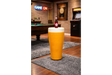 Round yellow Lager Side Table resembling a pint glass with white top, set on a grey rug in a game room.