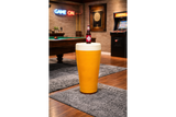 Round yellow Lager Side Table resembling a pint glass with white top, set on a grey rug in a game room.