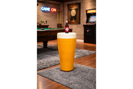 Round yellow Lager Side Table resembling a pint glass with white top, set on a grey rug in a game room.