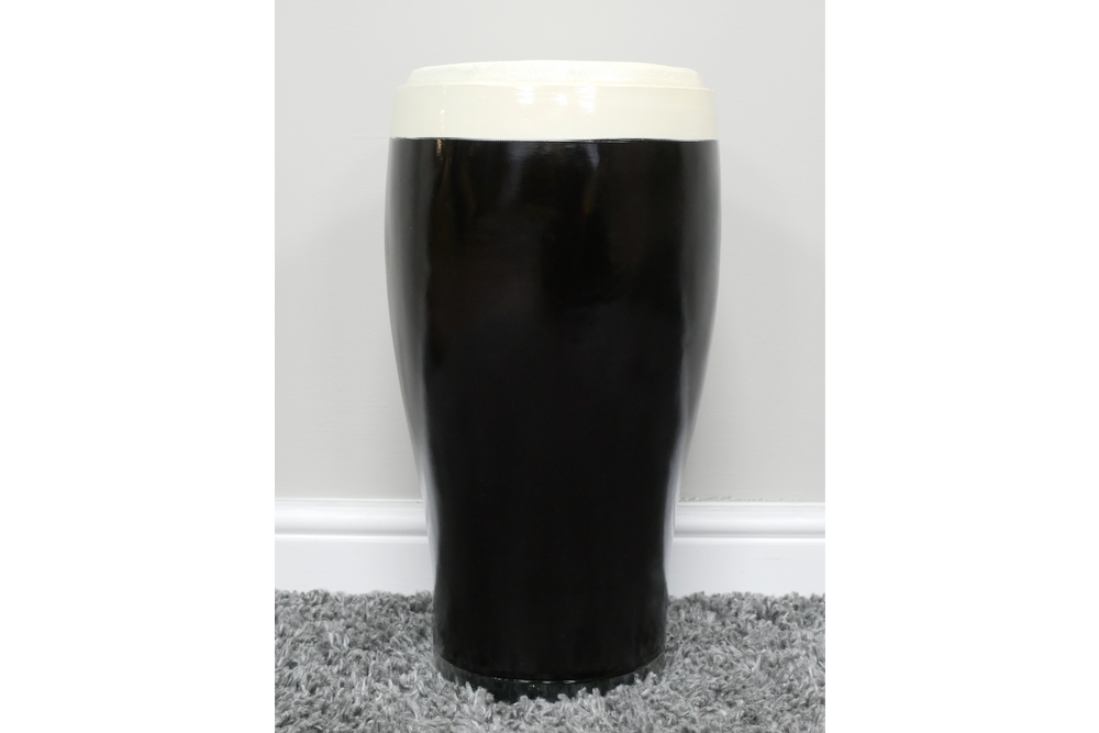 Black and white ceramic stout beer pint-shaped side table, front view on grey carpet against white wall.