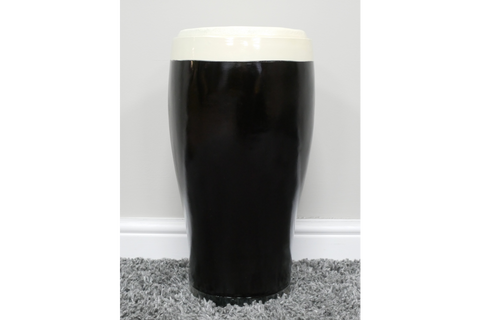 Black and white ceramic stout beer pint-shaped side table, front view on grey carpet against white wall.