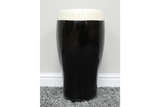 Black and white ceramic stout beer pint-shaped side table, front view on grey carpet against white wall.