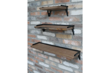 Set of 3 wooden wall shelves with black metal brackets mounted on a rustic brick wall, angled side view.