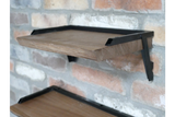 Set of 3 wall shelves with natural wood surfaces and black metal brackets mounted on a brick wall, side angle view.