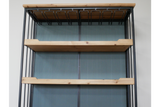 Bar cabinet with light wood shelves, black metal frame, and overhead wine glass holder, front view against gray wall.