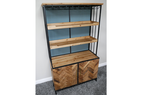 Bar cabinet with black metal frame, natural wood shelves and herringbone wood doors, angled view on gray carpet.