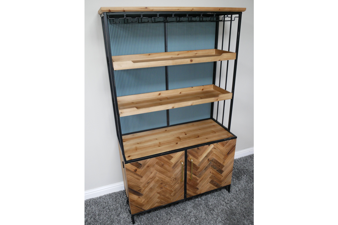 Bar cabinet with black metal frame, natural wood shelves and herringbone wood doors, angled view on gray carpet.
