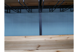 Close-up of light wood bar cabinet shelf with black metal wine glass racks hanging above, blue ribbed background.