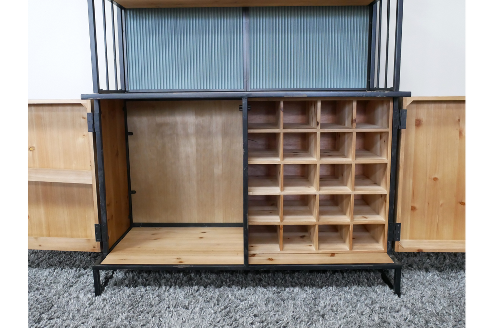 Wooden bar cabinet with black metal frame, open doors, divided bottle storage, and shelving on gray carpet.