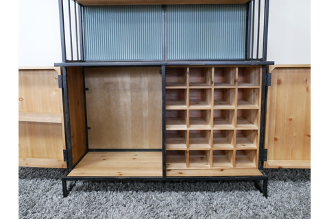 Wooden bar cabinet with black metal frame, open doors, divided bottle storage, and shelving on gray carpet.